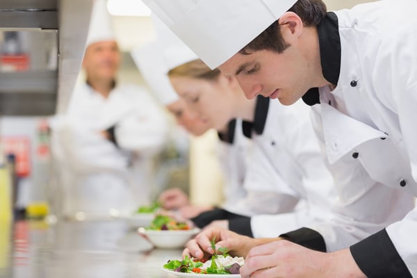 Culinary class in kitchen making salads as teacher is overlooking